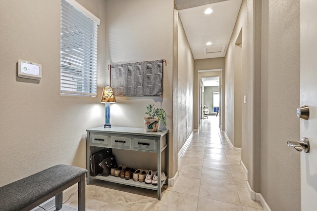 hallway with light tile patterned floors, attic access, and baseboards