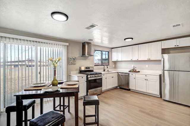 kitchen with sink, white cabinets, wall chimney range hood, light hardwood / wood-style floors, and stainless steel appliances