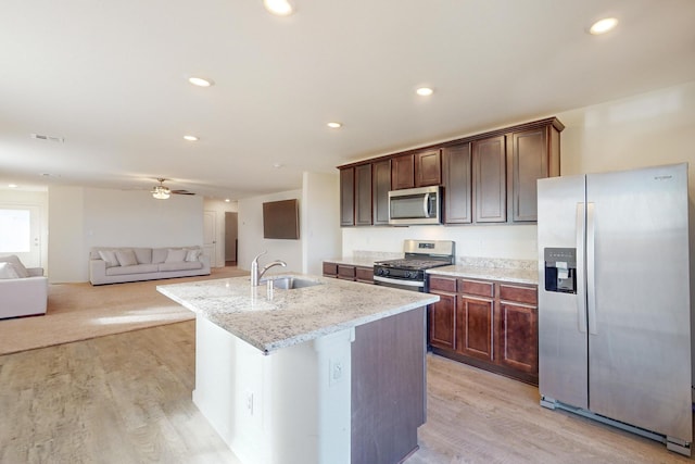 kitchen with light stone countertops, appliances with stainless steel finishes, light hardwood / wood-style floors, sink, and a kitchen island with sink