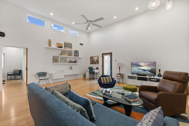 living room featuring ceiling fan, a towering ceiling, and light wood-type flooring