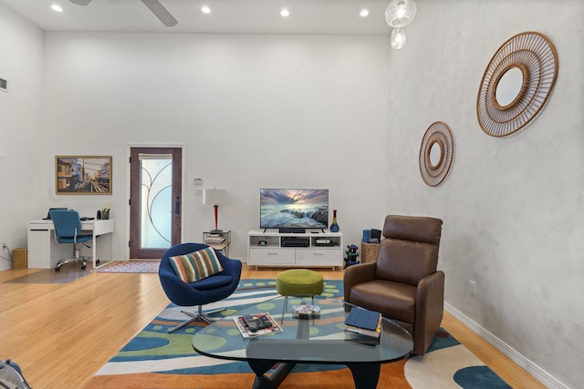 living room featuring ceiling fan, light hardwood / wood-style flooring, and a high ceiling