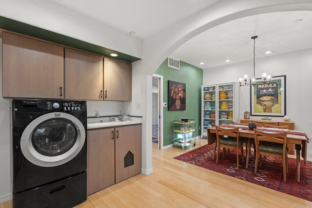 laundry area featuring washer / clothes dryer, a notable chandelier, light hardwood / wood-style flooring, and cabinets