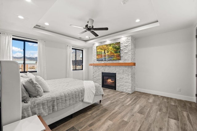 bedroom featuring wood-type flooring, a stone fireplace, ceiling fan, and a tray ceiling