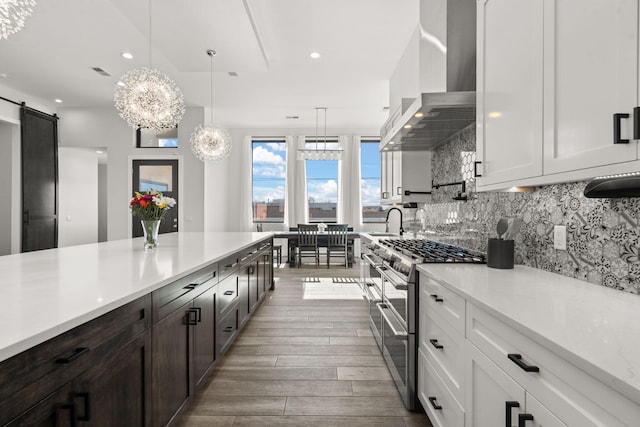 kitchen with decorative light fixtures, white cabinetry, range with two ovens, a barn door, and wall chimney exhaust hood