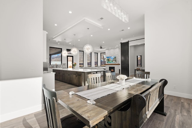 dining room with wood-type flooring, a barn door, ceiling fan, and a fireplace