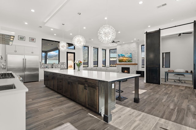 kitchen featuring decorative light fixtures, white cabinets, built in refrigerator, a barn door, and a spacious island