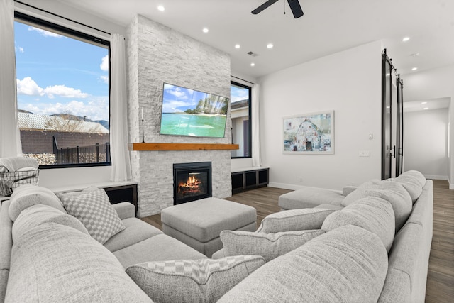 living room featuring a stone fireplace, dark wood-type flooring, and ceiling fan