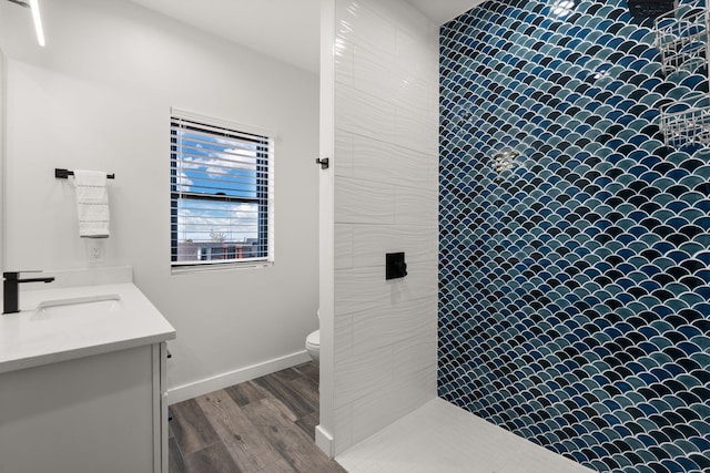 bathroom featuring vanity, a tile shower, hardwood / wood-style floors, and toilet