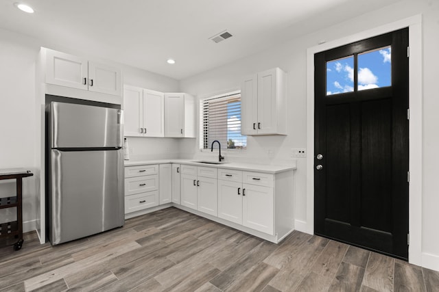 kitchen featuring white cabinetry, sink, stainless steel refrigerator, and light hardwood / wood-style flooring