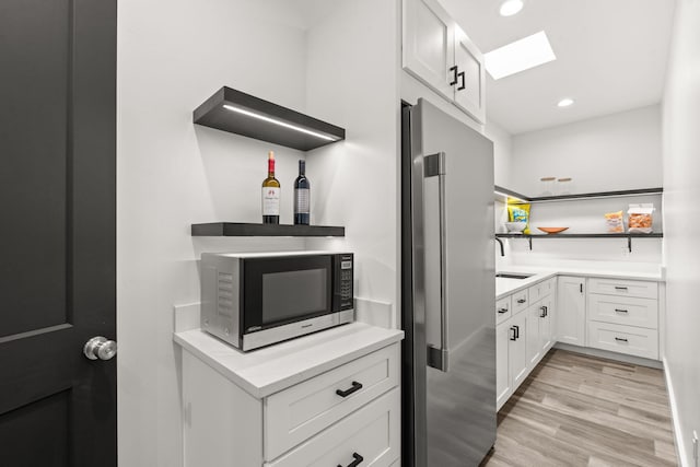 kitchen featuring white cabinetry, stainless steel appliances, a skylight, and light hardwood / wood-style flooring