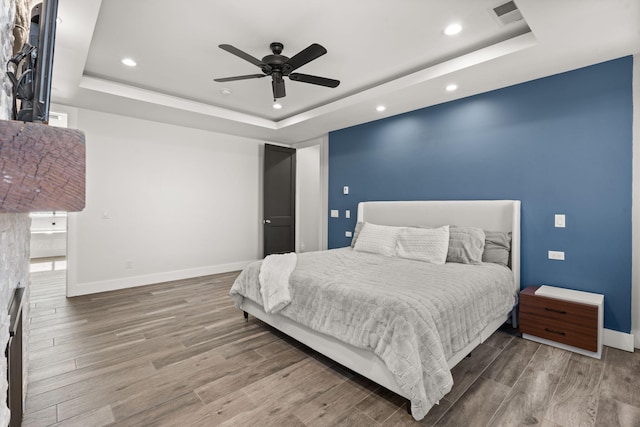 bedroom with ceiling fan, wood-type flooring, and a raised ceiling