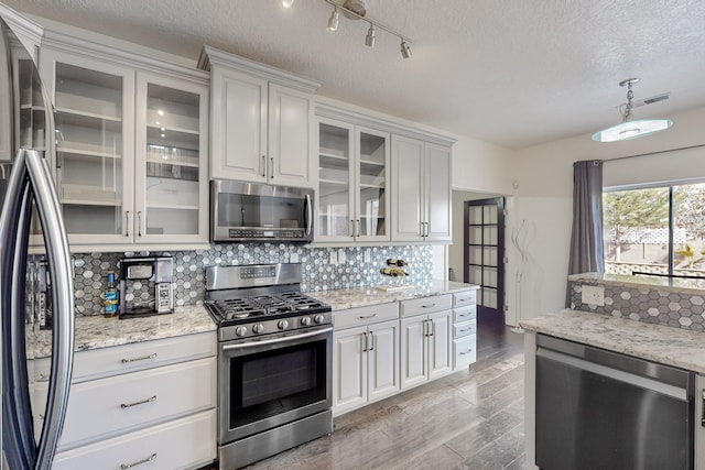 kitchen featuring pendant lighting, white cabinets, a textured ceiling, appliances with stainless steel finishes, and backsplash