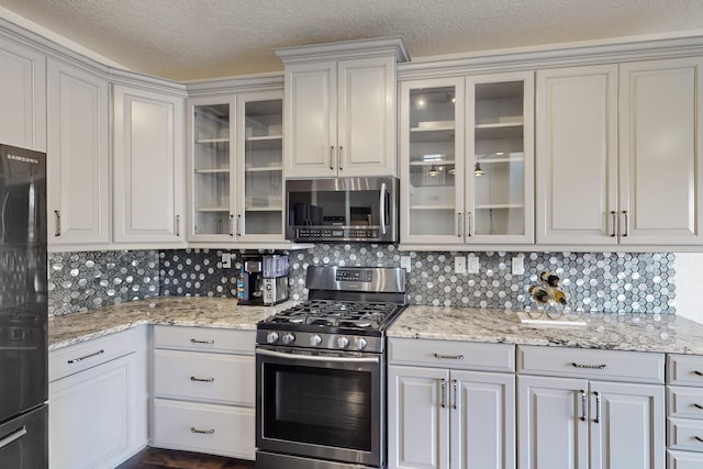 kitchen with a textured ceiling, decorative backsplash, white cabinetry, and appliances with stainless steel finishes