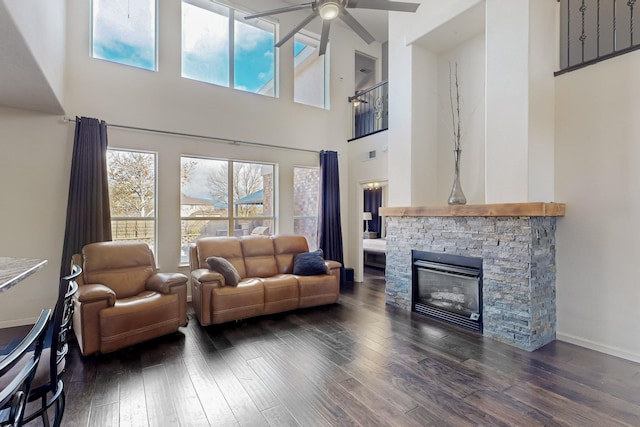 living room featuring a high ceiling, plenty of natural light, a stone fireplace, and dark wood-type flooring