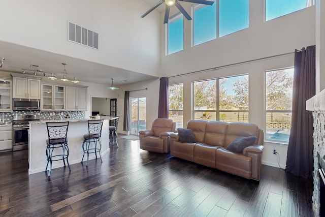 living room with ceiling fan, a high ceiling, and dark wood-type flooring