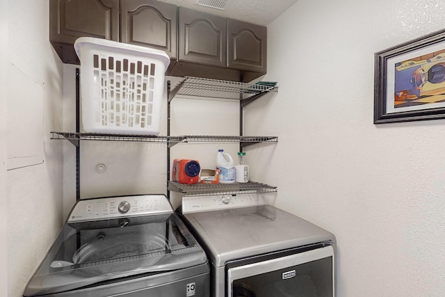 clothes washing area featuring cabinets, a textured ceiling, and separate washer and dryer