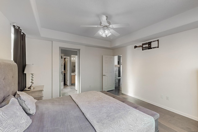 bedroom featuring ceiling fan, a tray ceiling, and light wood-type flooring