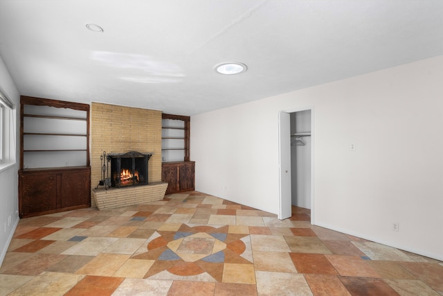 unfurnished living room featuring a brick fireplace and built in shelves