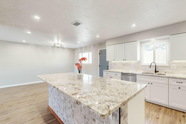 kitchen featuring visible vents, a kitchen island, dishwasher, decorative backsplash, and a sink