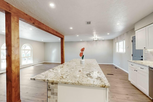 kitchen featuring a center island, light wood-type flooring, white cabinetry, and light stone counters