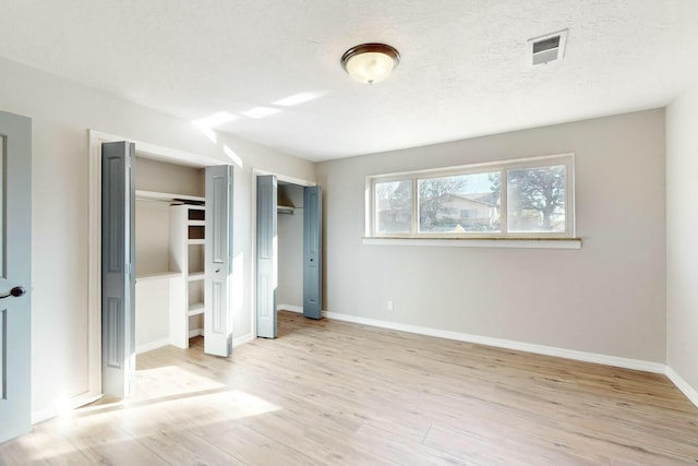 unfurnished bedroom featuring multiple closets, light hardwood / wood-style flooring, and a textured ceiling