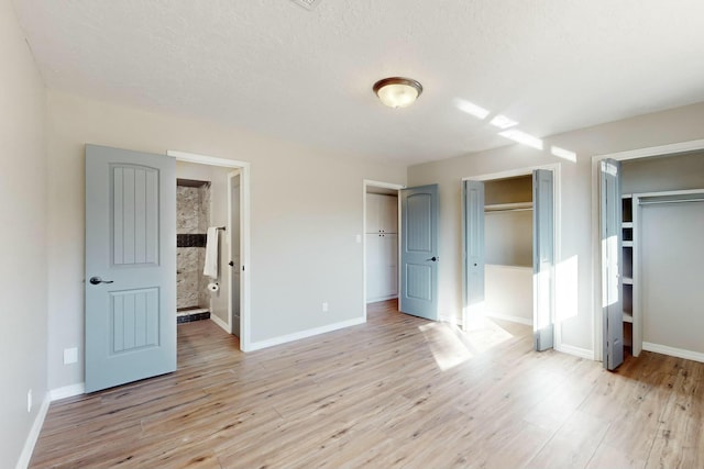 unfurnished bedroom featuring multiple closets, light hardwood / wood-style floors, and a textured ceiling