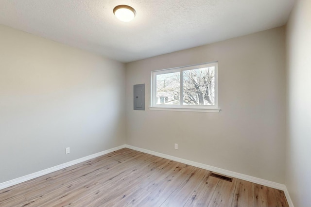 unfurnished room featuring a textured ceiling, light wood-type flooring, and electric panel