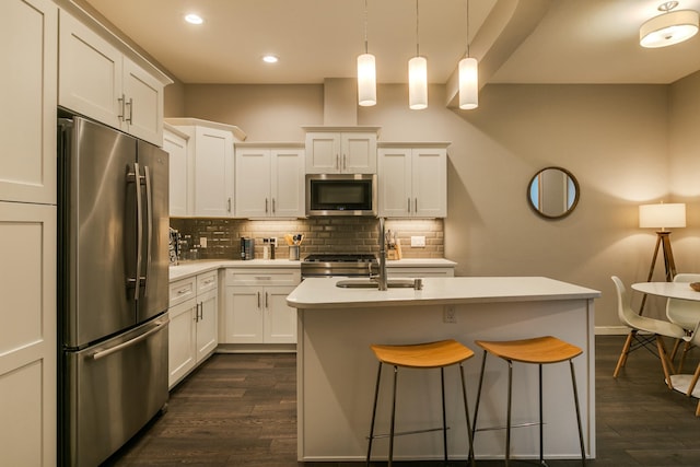 kitchen featuring stainless steel appliances, a center island with sink, white cabinets, and decorative light fixtures