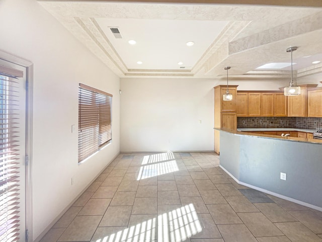 kitchen with pendant lighting, decorative backsplash, light tile patterned floors, and a tray ceiling