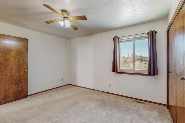 empty room featuring ceiling fan, light carpet, and a textured ceiling