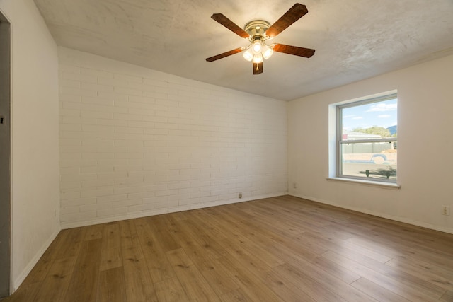 spare room with ceiling fan, brick wall, and light hardwood / wood-style floors