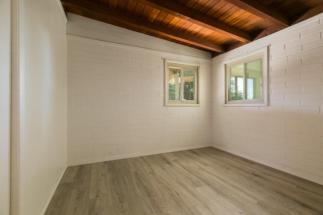 spare room featuring wood-type flooring, wooden ceiling, lofted ceiling with beams, and brick wall