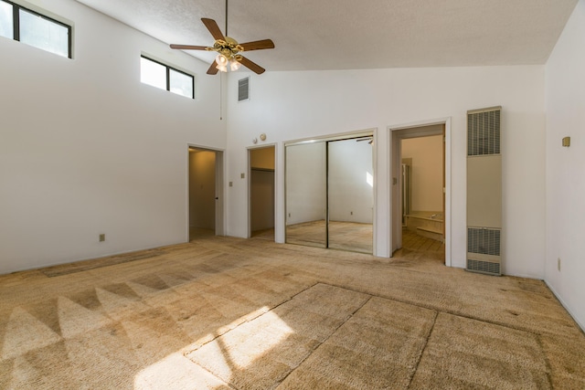 unfurnished bedroom featuring a high ceiling, ensuite bathroom, carpet, and ceiling fan