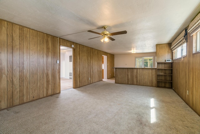 carpeted spare room with a textured ceiling, ceiling fan, and wood walls