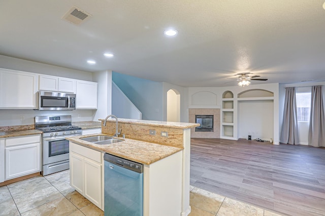 kitchen with white cabinetry, sink, a tiled fireplace, a kitchen island with sink, and stainless steel appliances