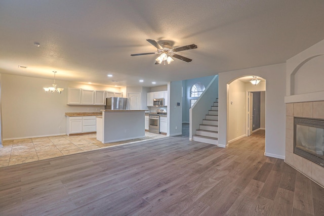 unfurnished living room featuring ceiling fan with notable chandelier, a fireplace, light hardwood / wood-style floors, and a textured ceiling