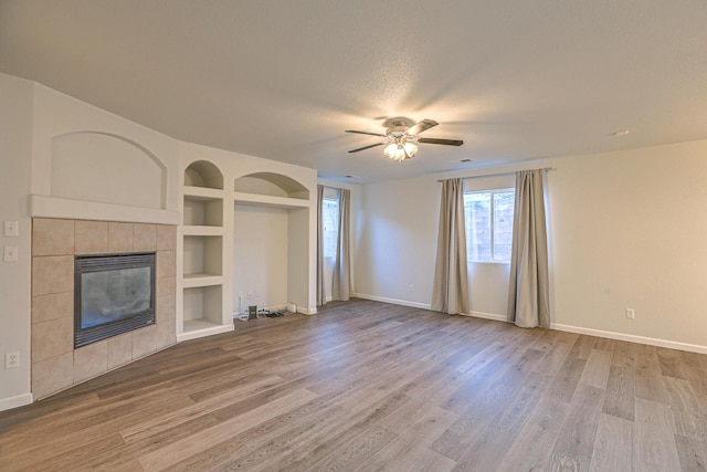 unfurnished living room with built in shelves, a textured ceiling, hardwood / wood-style flooring, ceiling fan, and a fireplace