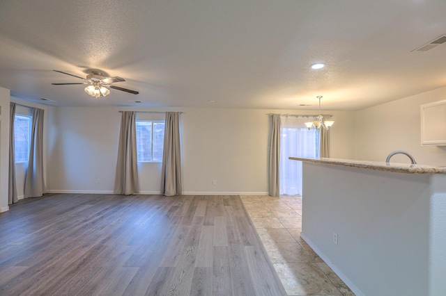 spare room with ceiling fan with notable chandelier, light hardwood / wood-style flooring, and a textured ceiling