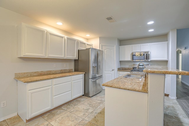 kitchen featuring sink, appliances with stainless steel finishes, white cabinetry, light stone counters, and a center island with sink