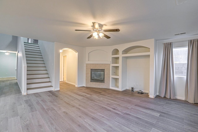 unfurnished living room with a tile fireplace, ceiling fan, light hardwood / wood-style floors, a textured ceiling, and built in shelves