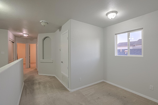 corridor with light carpet and a textured ceiling