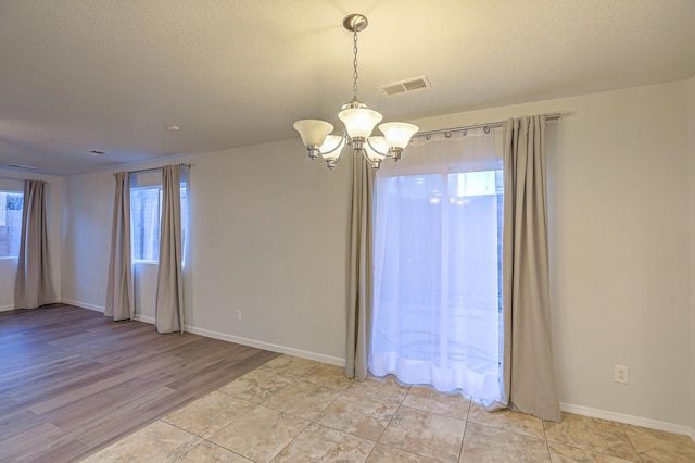 unfurnished room featuring a chandelier, a textured ceiling, and light hardwood / wood-style flooring