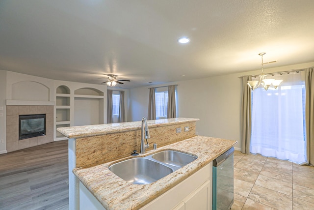 kitchen with sink, decorative light fixtures, a center island with sink, dishwasher, and light stone countertops