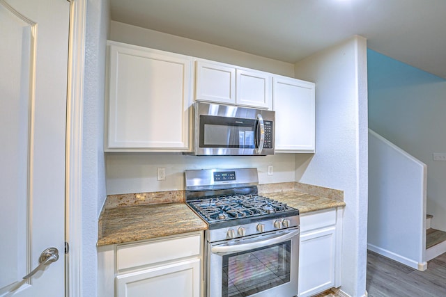 kitchen featuring white cabinetry, appliances with stainless steel finishes, wood-type flooring, and dark stone countertops