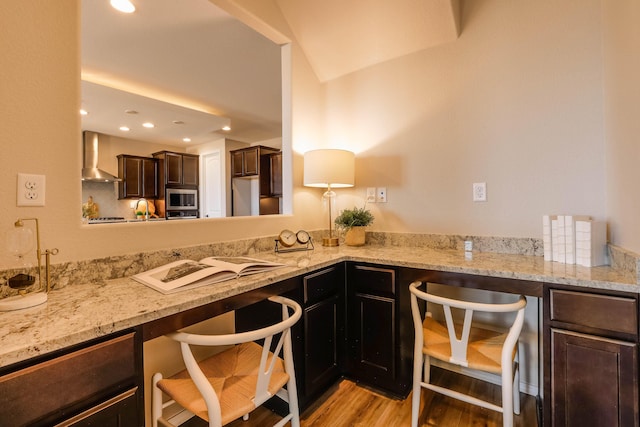 kitchen with light stone counters, freestanding refrigerator, stainless steel microwave, and wall chimney exhaust hood