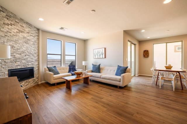 living room with recessed lighting, visible vents, a stone fireplace, and wood finished floors