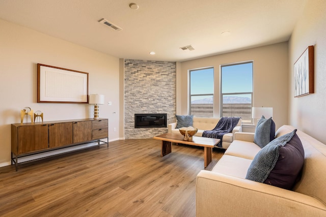 living room featuring a stone fireplace, light wood finished floors, a baseboard radiator, and visible vents