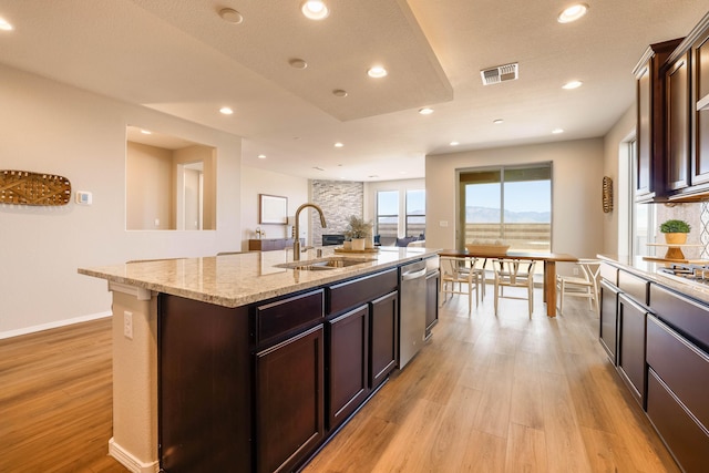 kitchen with visible vents, light wood-style flooring, a sink, and a center island with sink