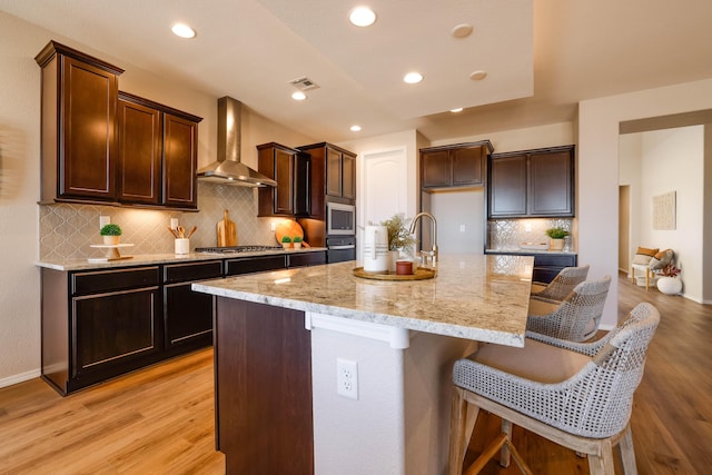 kitchen featuring a center island with sink, visible vents, a breakfast bar area, stainless steel appliances, and wall chimney range hood