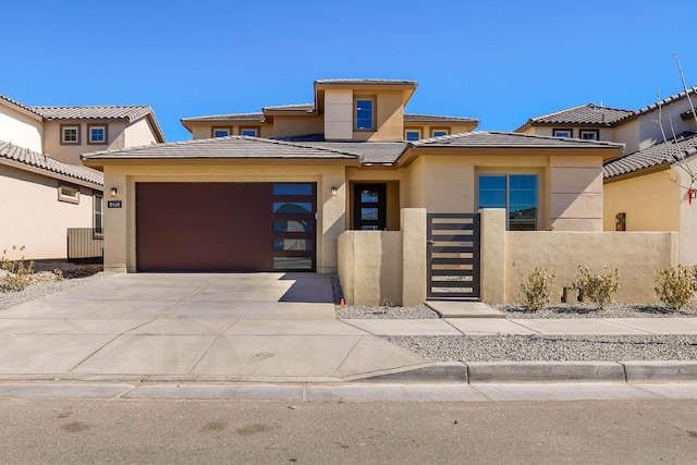 prairie-style home featuring concrete driveway, an attached garage, fence, and stucco siding